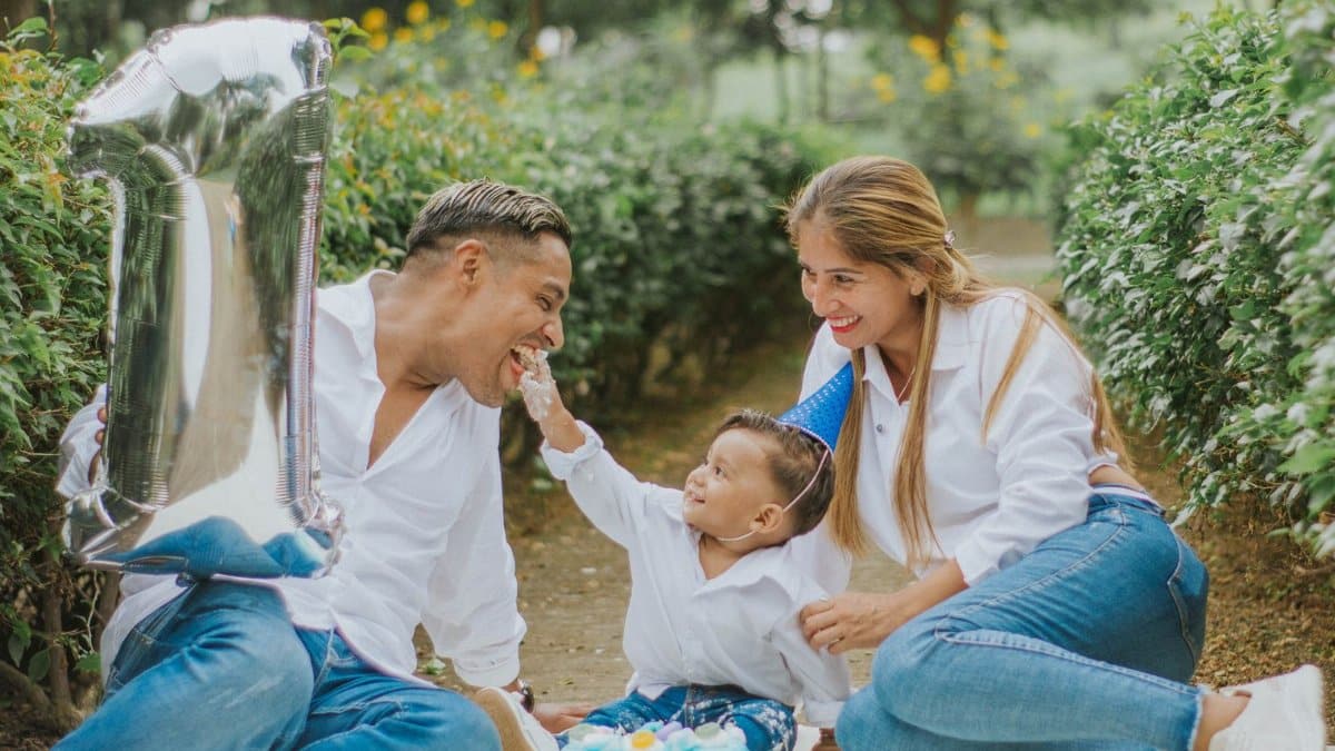 A joyful family celebrating their child's first birthday outdoors with cake and balloons.