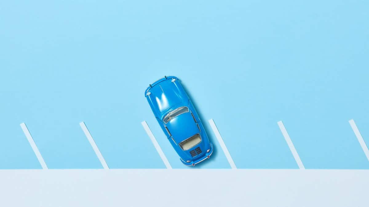 Overhead shot of a blue toy car in a parking slot on a pastel blue background.
