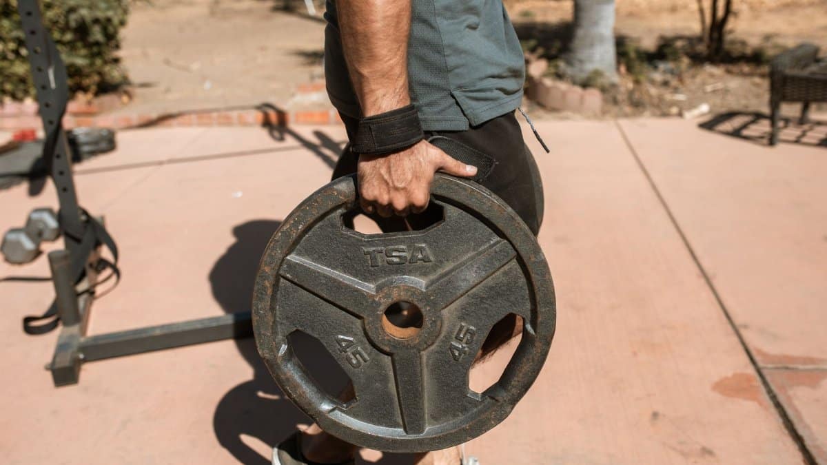 Close-up of a man's hand holding a 45lb weight plate outdoors during exercise.