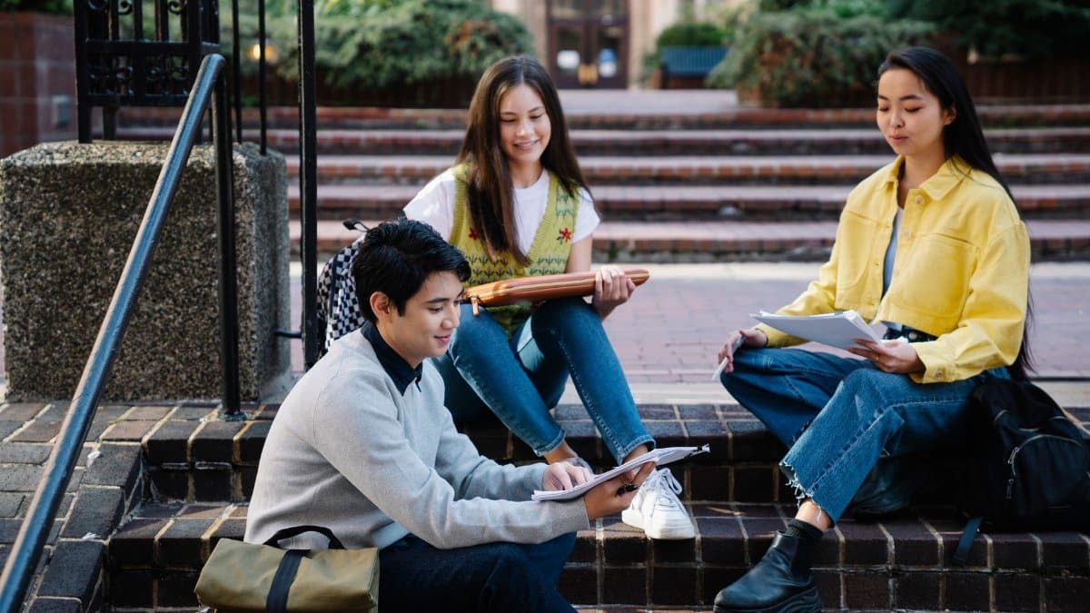 Group of students studying outdoors on college campus steps, enjoying sunny day.