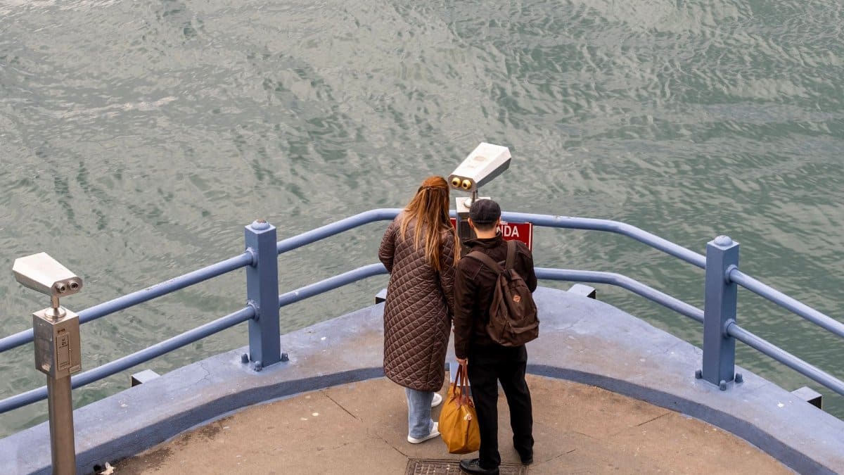 A couple stands on a waterfront deck, observing the serene water view, capturing a moment of outdoor leisure.