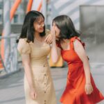 Two young women laughing and sharing a secret outdoors, exuding happiness and friendship.