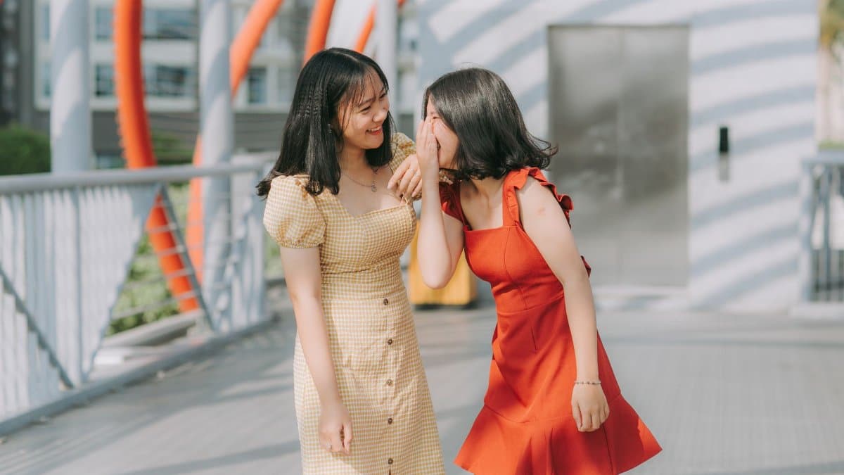 Two young women laughing and sharing a secret outdoors, exuding happiness and friendship.