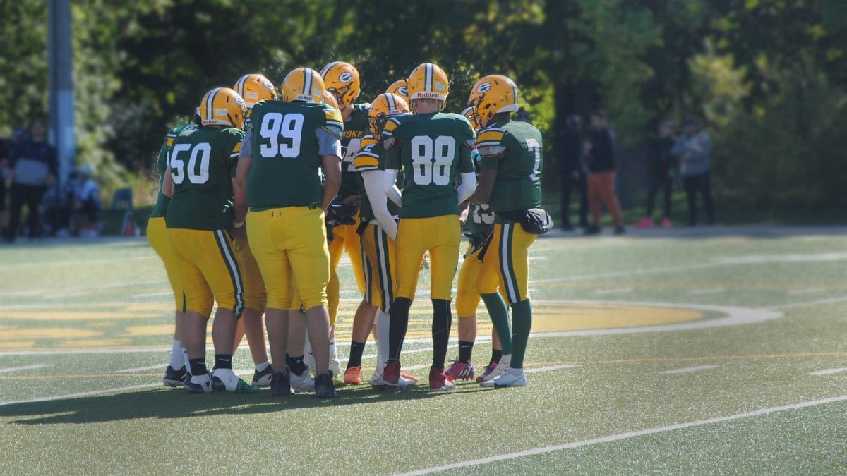 Group of football players in uniform huddling on an outdoor field, preparing for play.