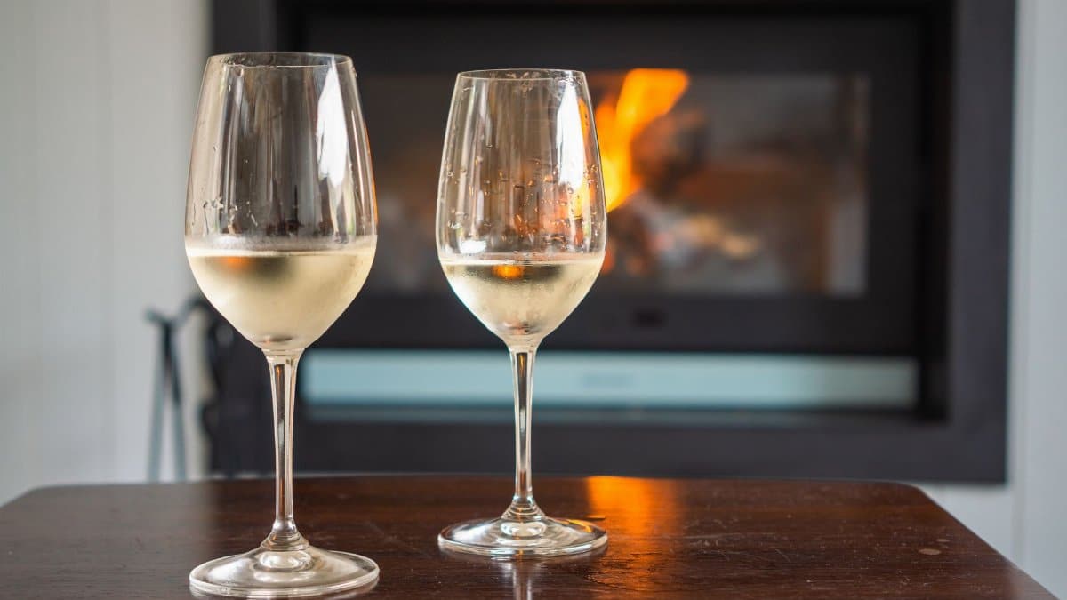 Two glasses of white wine in front of a warm fireplace, evoking a cozy atmosphere.