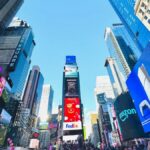 Vibrant daytime view of Times Square, showcasing iconic billboards and bustling crowd in New York City.