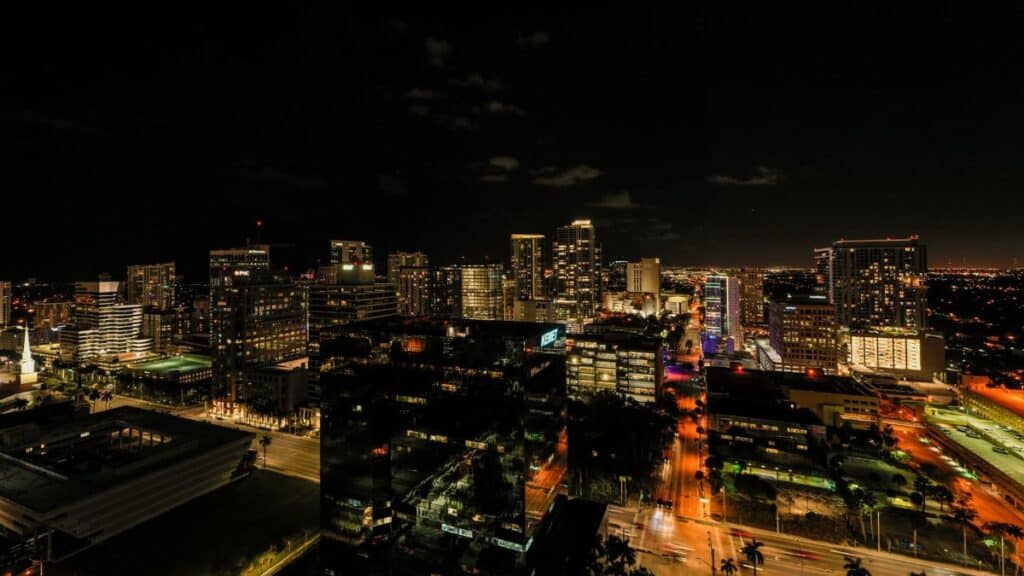 Drone view of asphalt roads and skyscrapers with glowing light and neon illumination in Fort Lauderdale at night