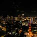 Drone view of asphalt roads and skyscrapers with glowing light and neon illumination in Fort Lauderdale at night