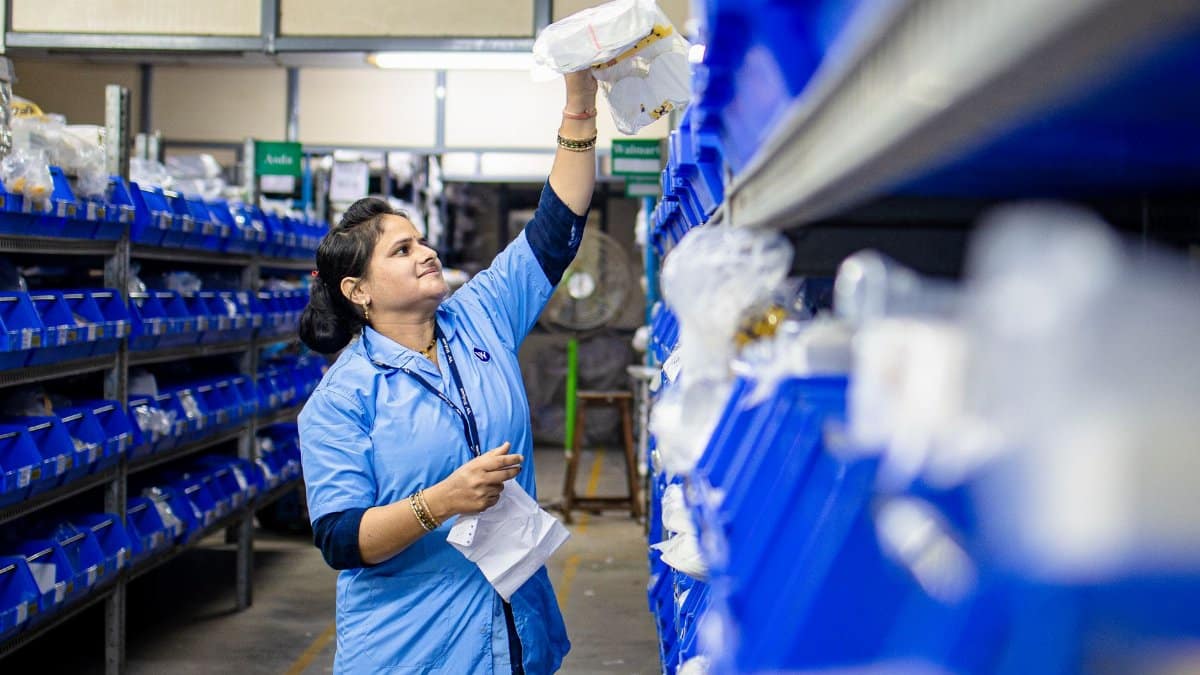 Female warehouse worker organizing inventory on blue industrial shelves. Efficient logistics management.