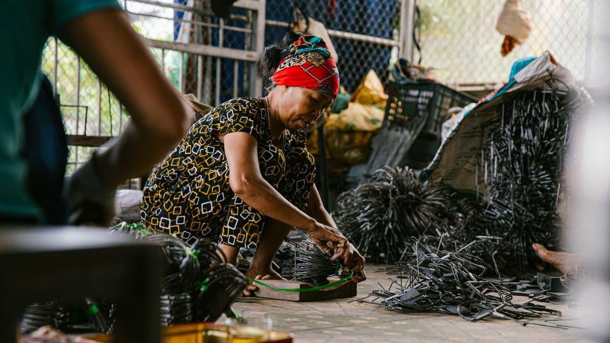 Focused woman working in a recycling center sorting metal parts on the floor.