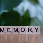 Wooden letter tiles spelling 'Memory' on a wooden table with blurred green background.