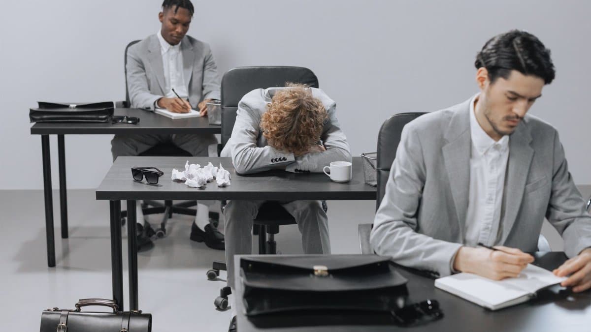 Tired employees in a modern office setting showing signs of workplace exhaustion.