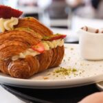 Mouthwatering croissant filled with cream and strawberries, served in a cozy cafe setting.
