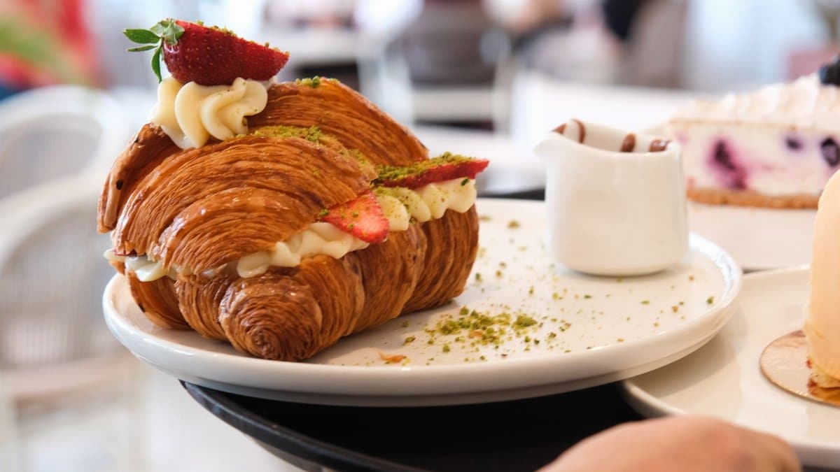 Mouthwatering croissant filled with cream and strawberries, served in a cozy cafe setting.