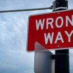 A close-up of a red wrong way road sign against an overcast sky, symbolizing caution.