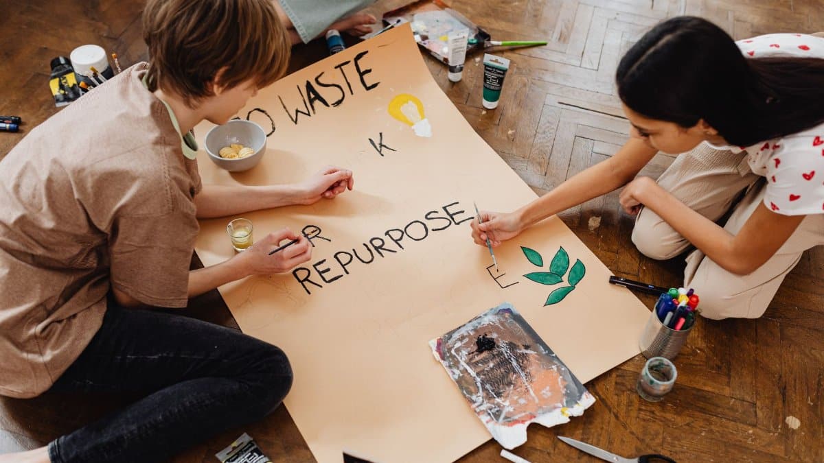 Two teenagers creatively paint a poster promoting eco-friendly practices like recycling and repurposing.