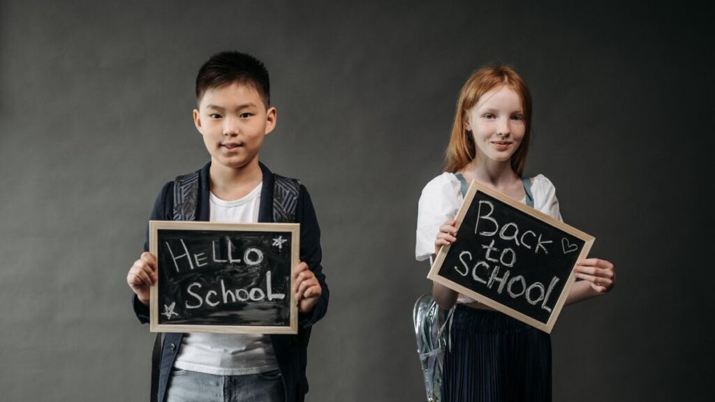 Two smiling students holding chalkboards with back to school messages.