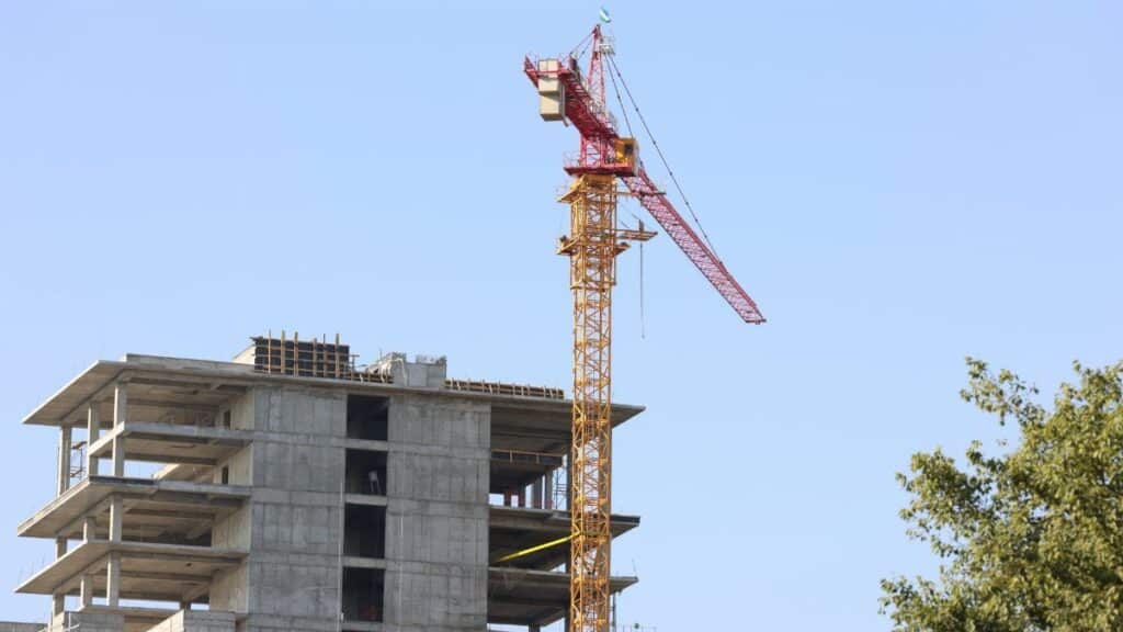 High-rise building under construction with crane in Oʻzbekiston cityscape.