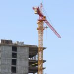 High-rise building under construction with crane in Oʻzbekiston cityscape.