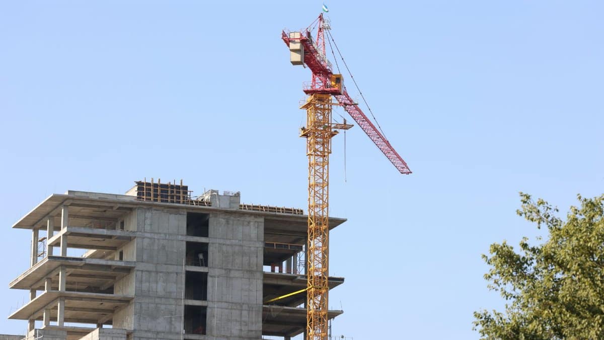 High-rise building under construction with crane in Oʻzbekiston cityscape.