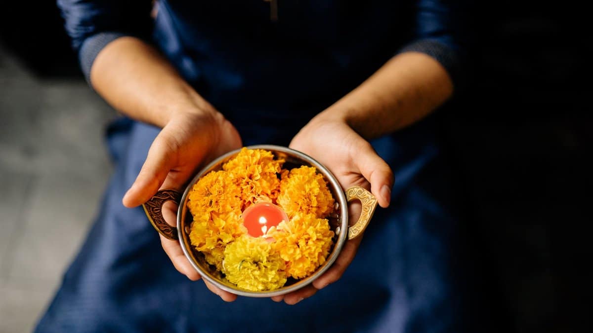 Hands holding a brass bowl with marigold flowers and a candle, symbolizing a Diwali ceremony.