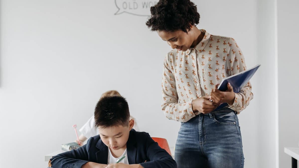 A teacher guides a student in a classroom, fostering an environment of learning and support.