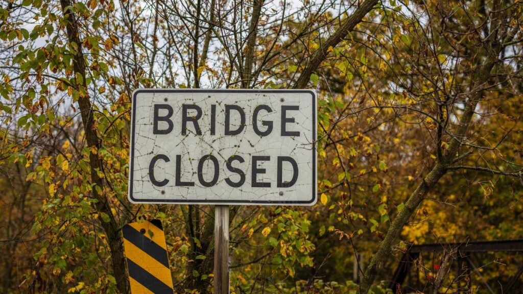 A 'Bridge Closed' sign amid autumn foliage indicating a road closure.