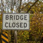 A 'Bridge Closed' sign amid autumn foliage indicating a road closure.