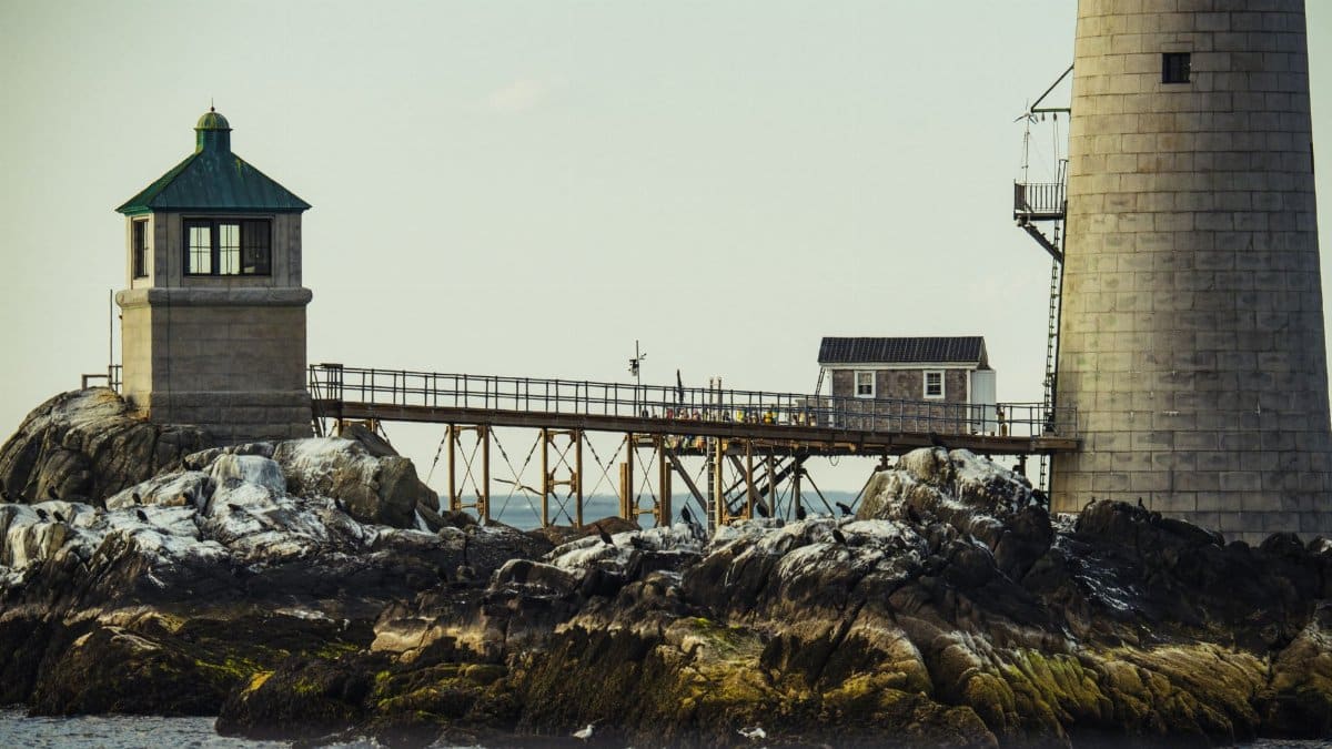 A scenic view of a lighthouse on rocky shores in Boston, MA.