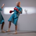Two children in hospital gowns engage in playful boxing in a well-lit room.