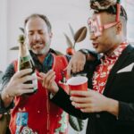 Two men celebrate in holiday style with champagne and festive attire.