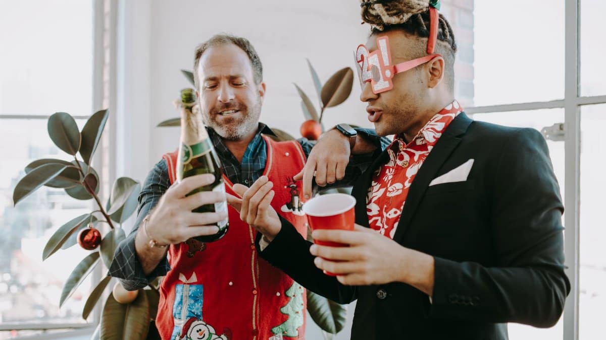 Two men celebrate in holiday style with champagne and festive attire.