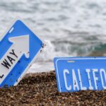 An artistic concept of California road signs partially buried in a beach with ocean waves.