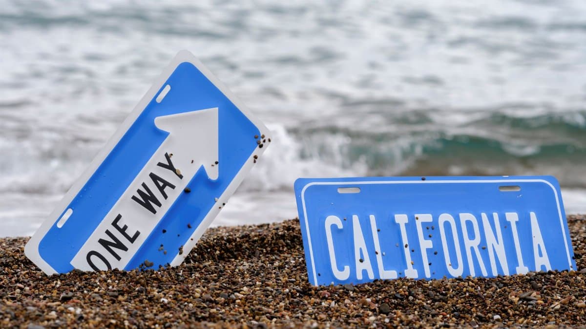 An artistic concept of California road signs partially buried in a beach with ocean waves.