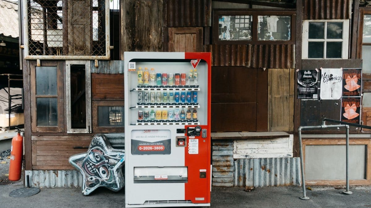 A vending machine stands in front of an eclectic wall with corrugated metal and old wood panels.
