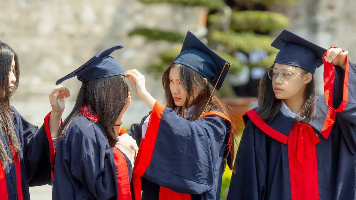 Group of young Asian women celebrating graduation outdoors in academic gowns.
