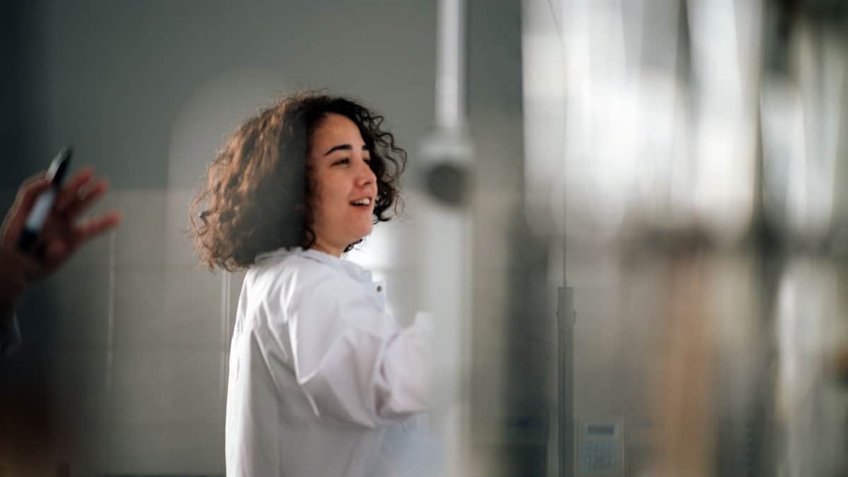 A young female scientist with curly hair in a lab coat working in a laboratory setting.