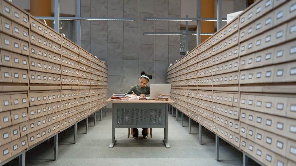 Student diligently studies at a desk surrounded by library card catalogs, focusing on her work.