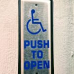 Close-up of a push button sign for accessibility on a white wall.
