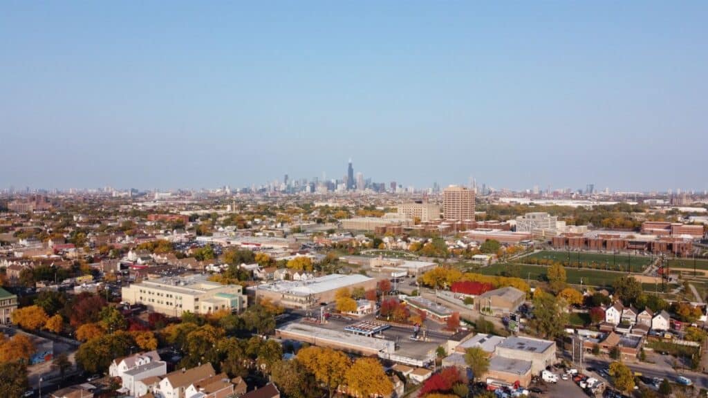 Drone shot capturing the sprawling Chicago skyline with colorful suburban landscape in the foreground.