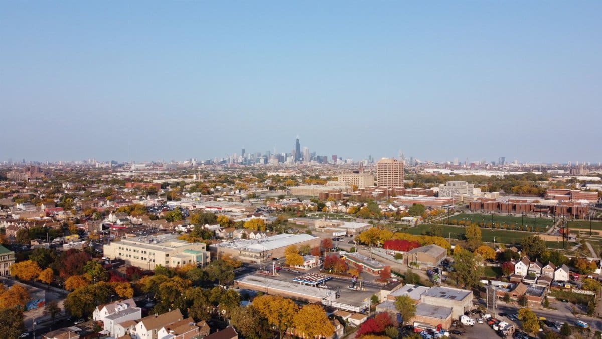 Drone shot capturing the sprawling Chicago skyline with colorful suburban landscape in the foreground.