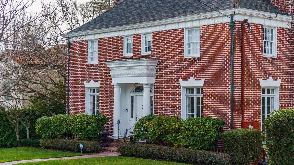 Elegant traditional red brick home with lush garden, showcasing classic American architecture.