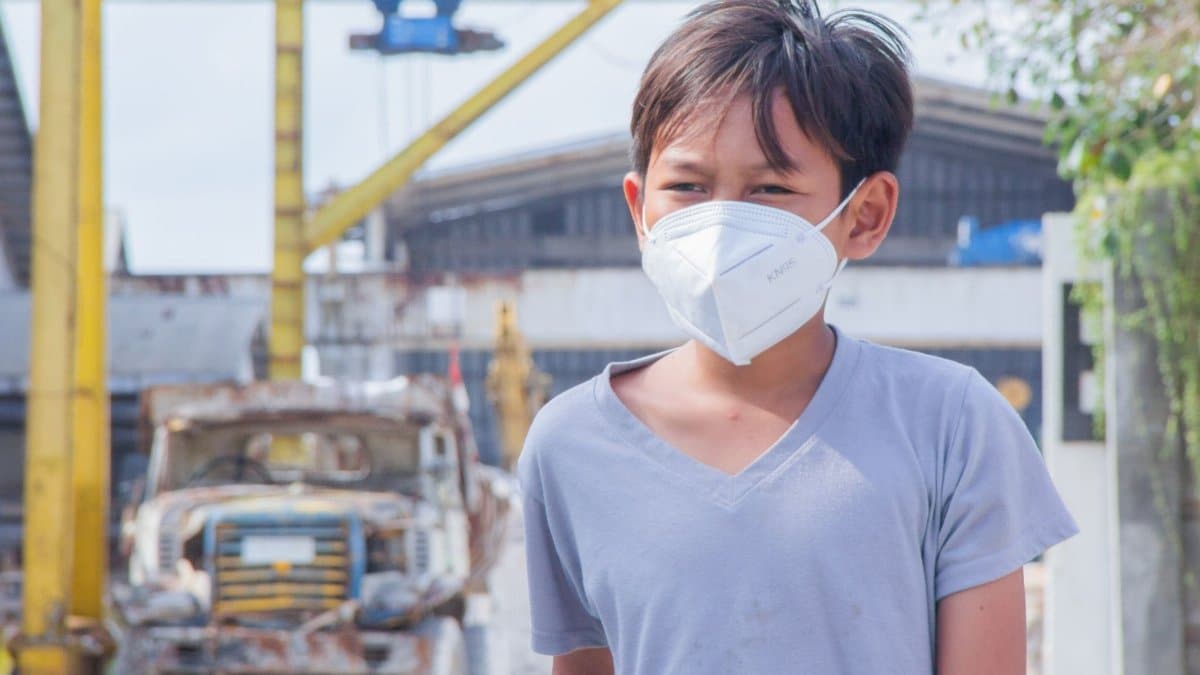 A young boy wearing a face mask stands in an industrial setting, highlighting safety during the pandemic.
