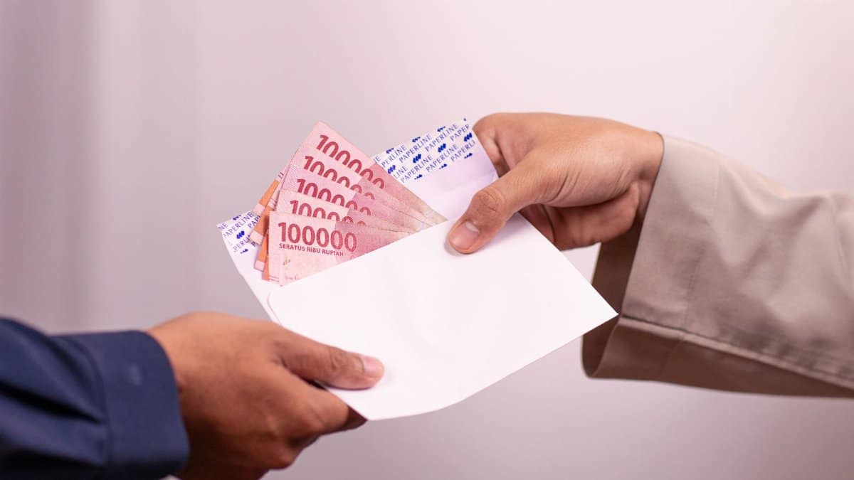Hands giving and receiving Indonesian rupiah in an envelope, symbolizing financial transaction.