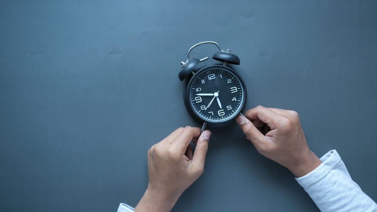 Hands adjusting a classic black alarm clock on a blue background with ample copy space.