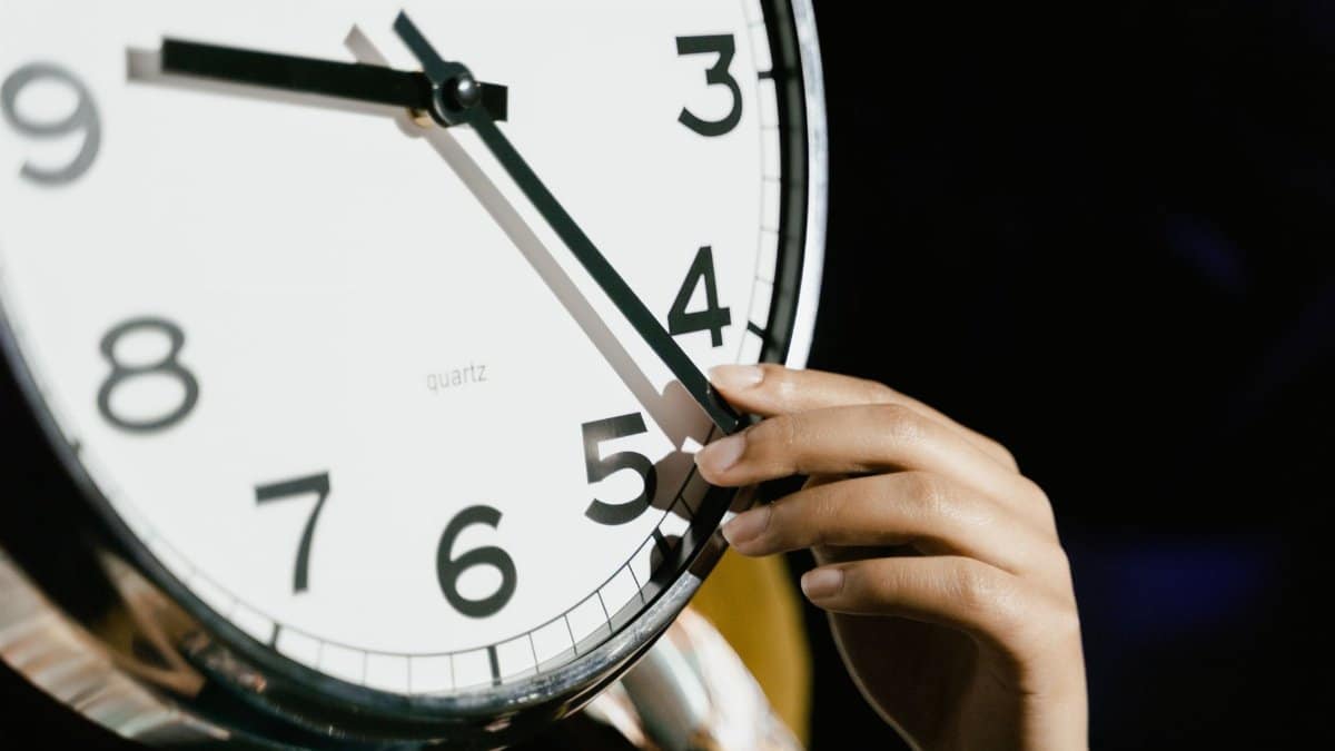 A hand adjusting the time on a large analog clock with bold numbers.