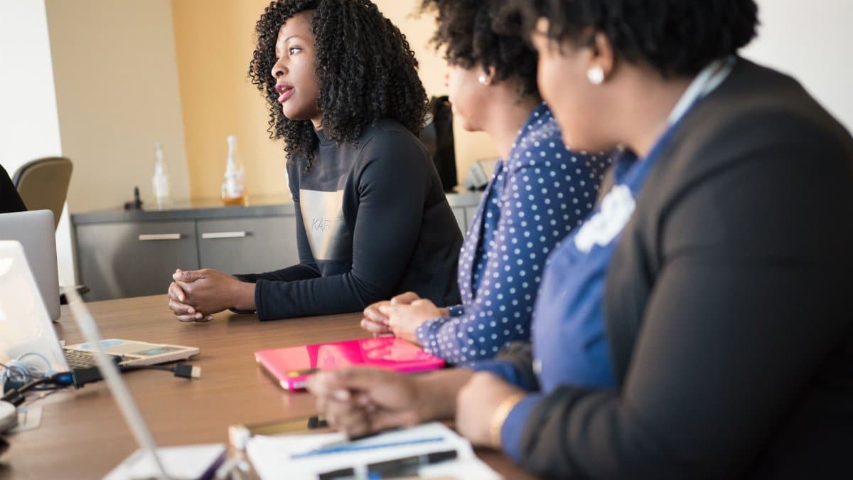 A group of women engaged in a professional meeting, collaborating in a modern office setting with laptops and documents.