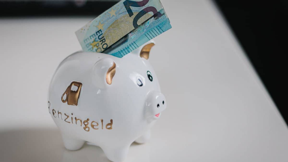 A white piggy bank with a €20 note inserted, symbolizing savings.