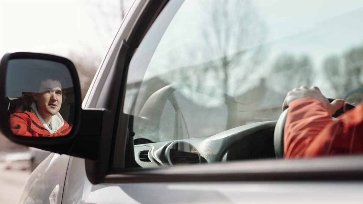 Close-up of a man reflected in a car side mirror while driving on a sunny day.
