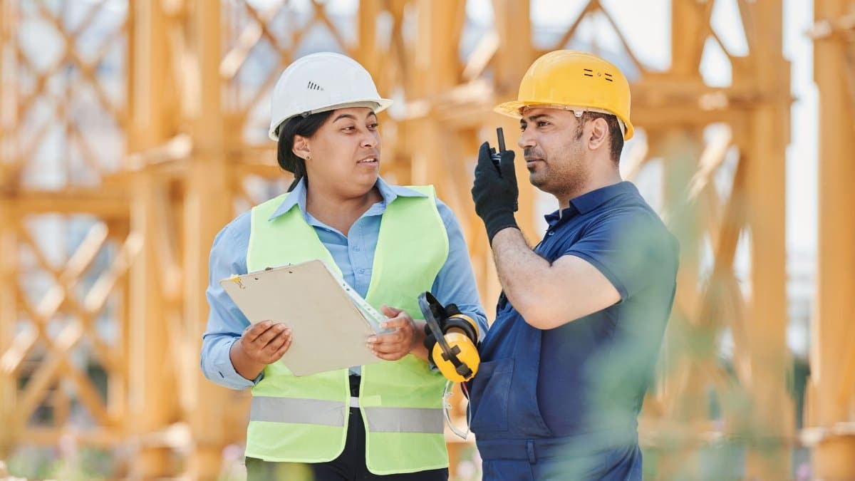 Engineers in safety gear discussing a construction project outdoors with visible scaffolding.